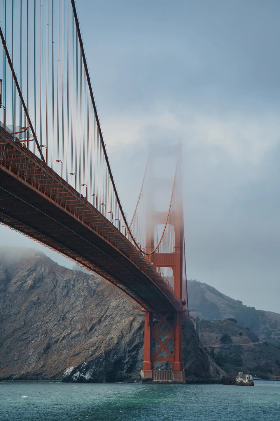 The Golden Gate Bridge seen from below, its far tower fading into fog over the bay